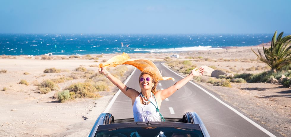 Mulher de férias com um carro no meio da estrada e o mar ao fundo