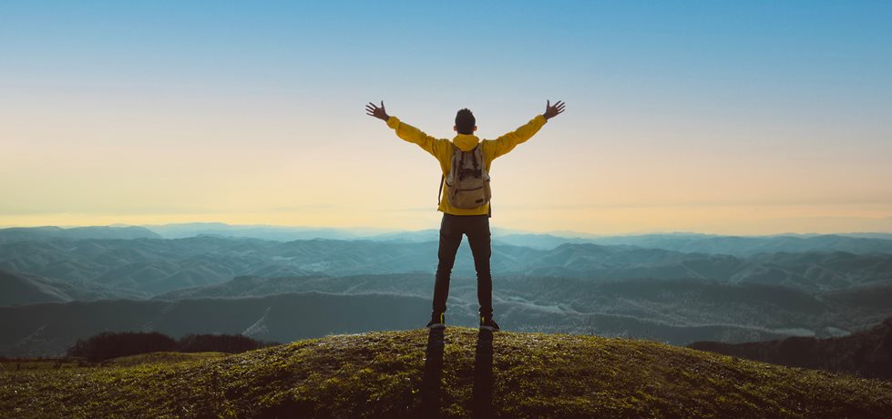 Homem com os braços abertos no topo da montanha