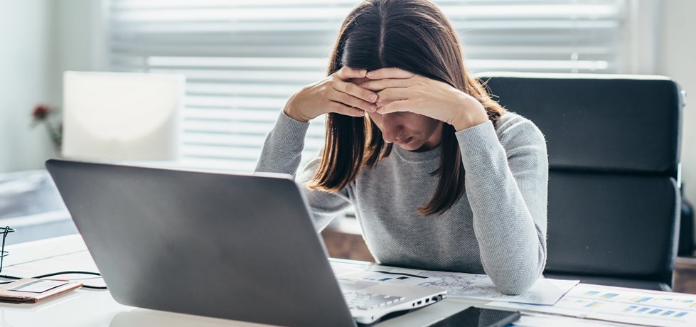 Mulher sentada à mesa no escritório, inclinando a cabeça na mão com os olhos para baixo.