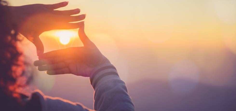 A mulher fazendo moldura ao redor do sol com as mãos no nascer do sol